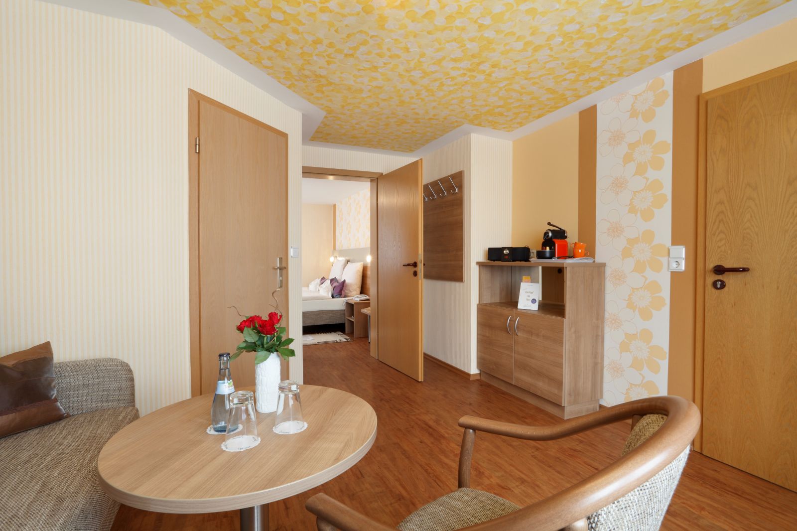 Eingangsbereich der Suite mit Sitzecke, Tisch, Kaffeemaschine und Blick ins Schlafzimmer
